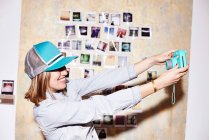 Jovem mulher na frente da parede da foto tirando selfie instantânea — Fotografia de Stock