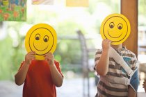 Two boys holding up smiley face masks at nursery school — Stock Photo