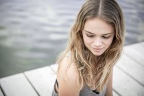 Молодая женщина сидит на пристани, смотрит в сторону — стоковое фото