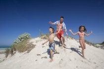 Homem adulto médio correndo na duna de areia com filho e filha na praia, Maiorca, Espanha — Fotografia de Stock