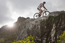 Joven ciclismo de montaña en la cima de la formación de rocas - foto de stock