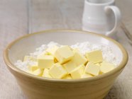 Butter cubes and flour in mixing bowl — Stock Photo