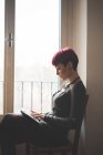 Junge Frau sitzt am Fenster und nutzt digitales Tablet — Stockfoto