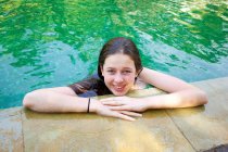 Chica en la piscina apoyada en la piscina - foto de stock