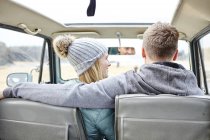 Visão traseira do jovem casal no carro na praia — Fotografia de Stock