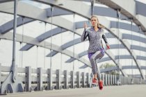 Бегущая женщина на скорости по городскому пешеходному мосту — стоковое фото