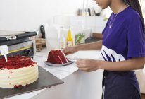 Официантка режет красный бархатный торт у стойки кафе — стоковое фото