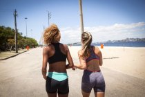 Дві молоді жінки біжать на пляжі, вид ззаду — стокове фото