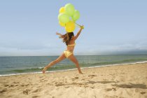Frau springt mit Luftballons am Strand — Stockfoto