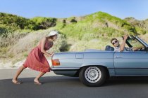 Frau schubst Auto, während Freund lenkt — Stockfoto
