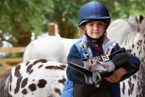 Young girl holding a saddle with ponies — Stock Photo