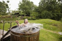 Mature woman jumping into fresh cold water tub at eco retreat — Stock Photo