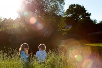 2 young kids sitting in long grass. — Stock Photo