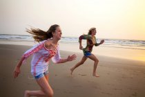 Mãe e filha correndo na praia ao pôr do sol — Fotografia de Stock