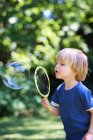 Мальчик надувает огромный пузырь на заднем дворе — стоковое фото