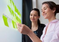Female colleagues sticking adhesive notes on glass — Stock Photo