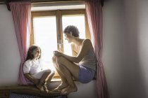 Junge Frau und Tochter sitzen auf Fensterbank — Stockfoto