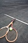 Tennis rackets and ball on court under net — Stock Photo