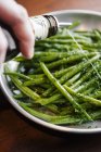 Person pouring sauce on green beans — Stock Photo