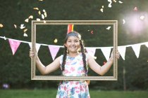 Portrait of girl looking through picture frame, smiling at camera — Stock Photo