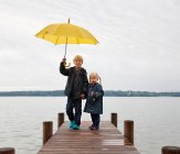Children with yellow umbrella on dock — Stock Photo
