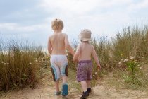 Niños tomados de la mano en arena herbácea - foto de stock