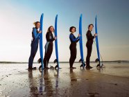 Cuatro surfistas femeninas de pie en una playa - foto de stock