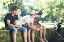Meninos sentados na parede e pesca na lagoa — Fotografia de Stock