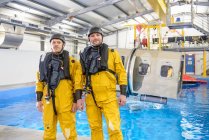 Retrato de trabajadores petroleros offshore entrenando en instalaciones de piscina con simulador de helicóptero en el fondo - foto de stock