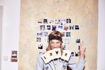 Young woman in front of photo wall holding up love and peace signs — Stock Photo