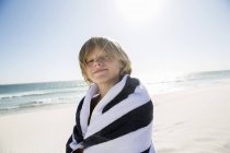 Хлопчик на пляжі, загорнутий в смугастий рушник, дивиться на камеру — стокове фото