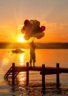 Boy holding balloons on wooden dock — Stock Photo
