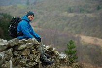Hiking man sitting on stone wall — Stock Photo