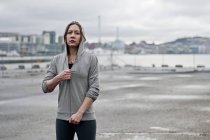 Portrait of young female runner zipping hoody on dockside — Stock Photo