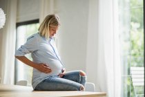 Повна вагітність молода жінка сидить на кухонному столі — стокове фото
