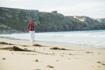 Donna matura che messaggia su smartphone mentre passeggia sulla spiaggia, Camaret-sur-mer, Bretagna, Francia — Foto stock