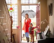 Madre e hijo que llegan a la puerta principal del hogar en el día lluvioso, retrato - foto de stock
