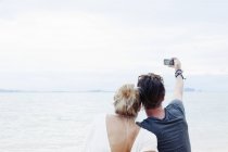 Vista posteriore della giovane coppia scattare selfie smartphone sulla spiaggia, Kradan, Thailandia — Foto stock