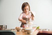 Girl sieving flour into mixing bowl — Stock Photo