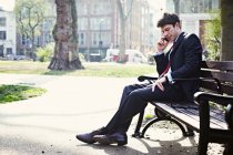 Бізнесмен сидить на лавці парку, розмовляючи на мобільному телефоні — стокове фото