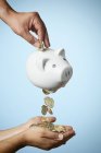 Close-up tiro de mão colocando moeda em porquinho banco e moedas fluindo para fora no fundo de cor — Fotografia de Stock