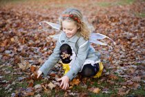 Ragazza in ali di fata che gioca in foglie a parco — Foto stock