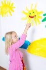 Chica joven pintura sonriente sol en la pared - foto de stock