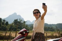 Mujer fotografiándose en ciclomotor, Vang Vieng, Laos - foto de stock