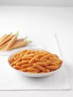 Raw carrots on marble cutting board and bowl of boiled carrots — Stock Photo