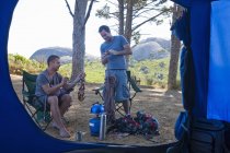 Двое молодых людей беседуют и готовят лагерь перед палаткой — стоковое фото