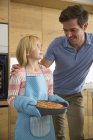 Menina carregando bolo de maçã caseiro sem glúten para o pai na cozinha — Fotografia de Stock
