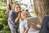 Дружина дивиться чоловіка за допомогою цифрового планшета на гамаку — стокове фото