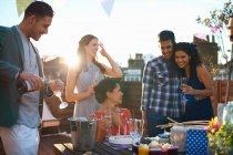 Друзья на вечеринке на террасе на крыше наливают шампанское — стоковое фото