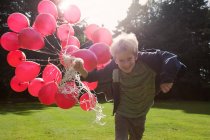 Boy carrying bunch of balloons outdoors — Stock Photo